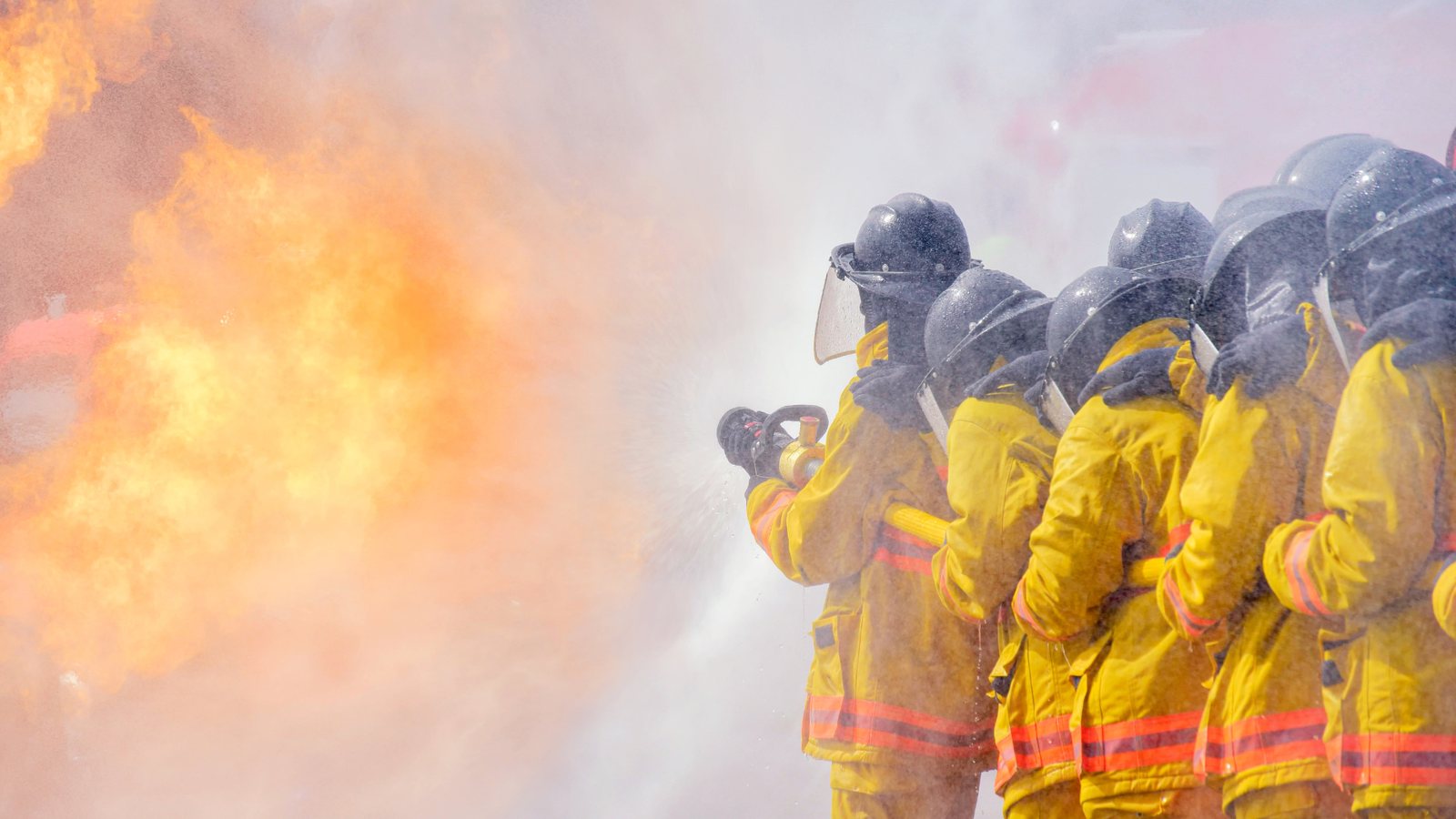Firefighters directing a hose onto a large live training fire